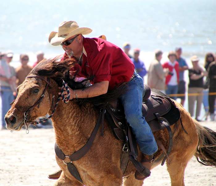 Мужчина в ковбойской шляпе скачет на лошади держась за ее шею, фото фотография